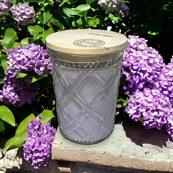glass candle with wood top on a concrete shelf surrounded by fresh purple lilacs