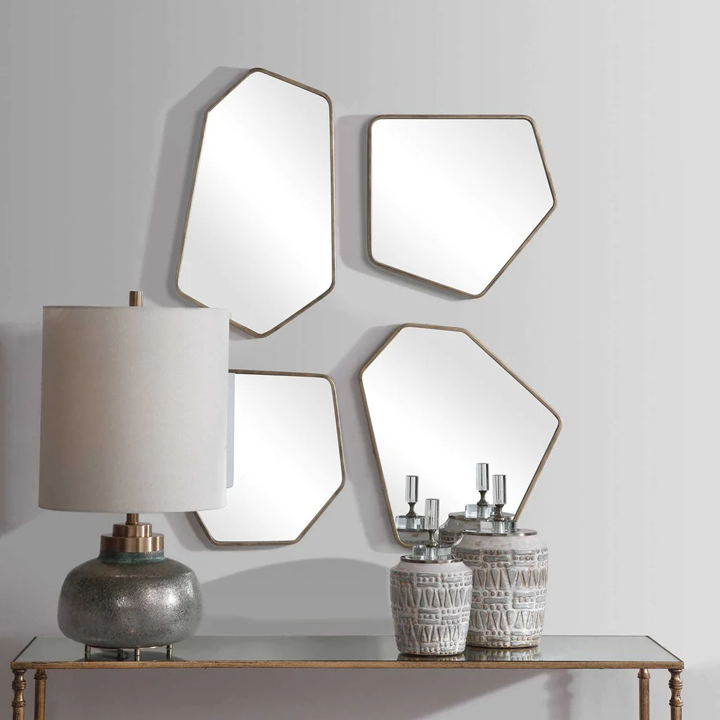 four unique multi-sided mirrors arranged on a wall behind a table with vases and a lamp