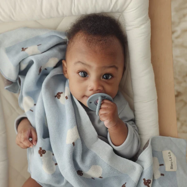 dark skin baby wrapped in a light blue blanket with sheep print