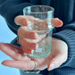 Hand holding a small glass with water against a blue background