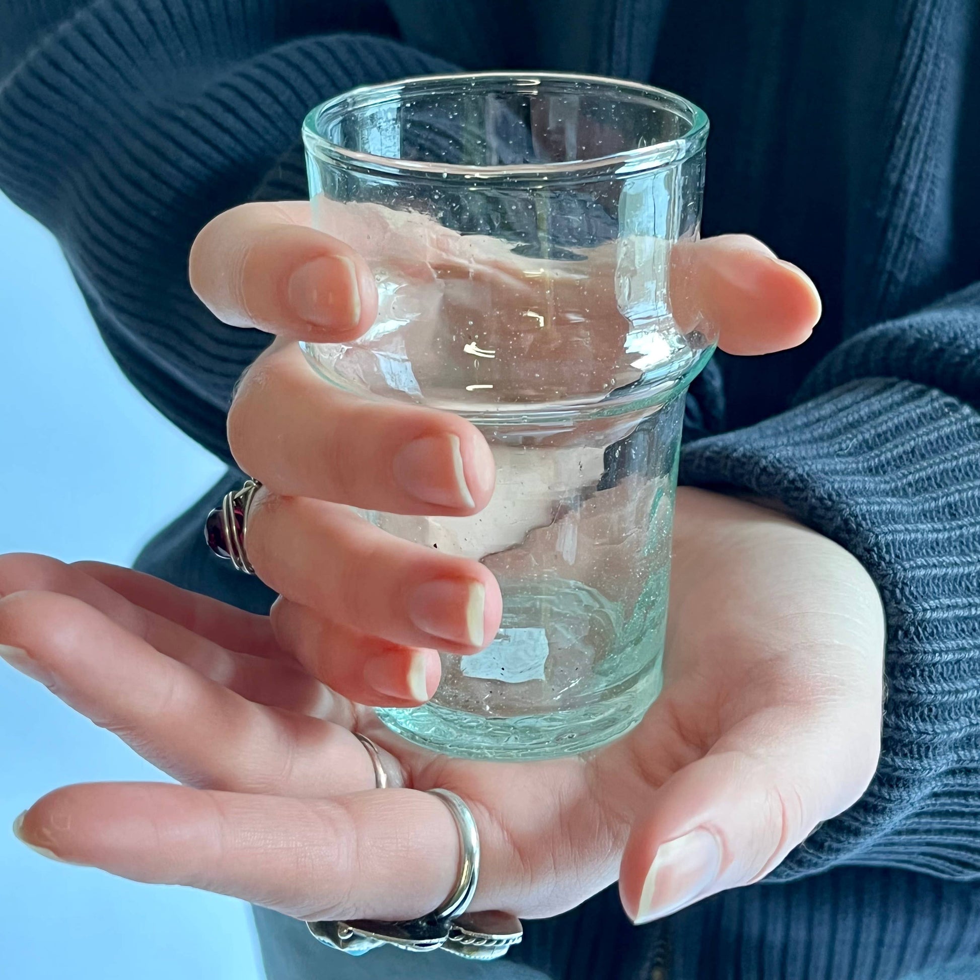 Hand holding a small glass with water against a blue background