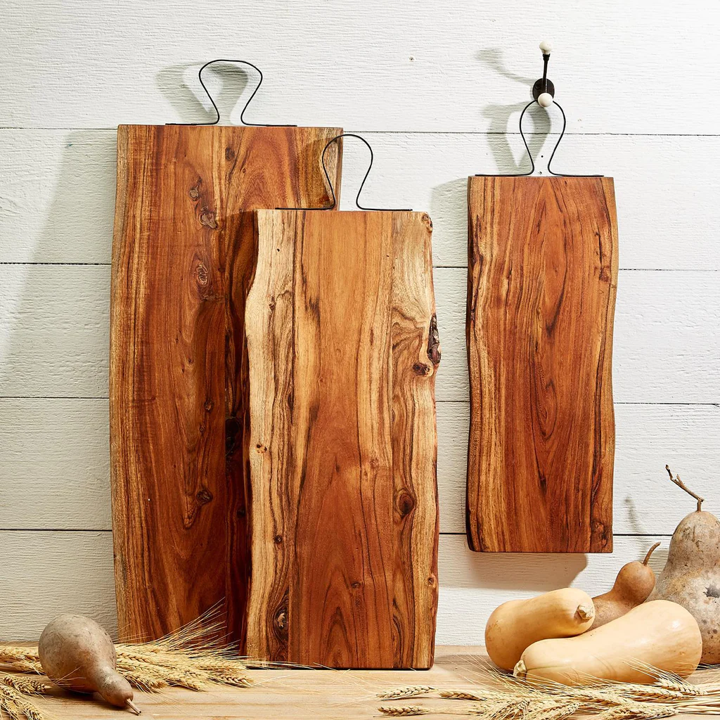 three live edge wooden cutting boards standing vertically with metal handles and autumn squash and pears on the counter where they are displayed