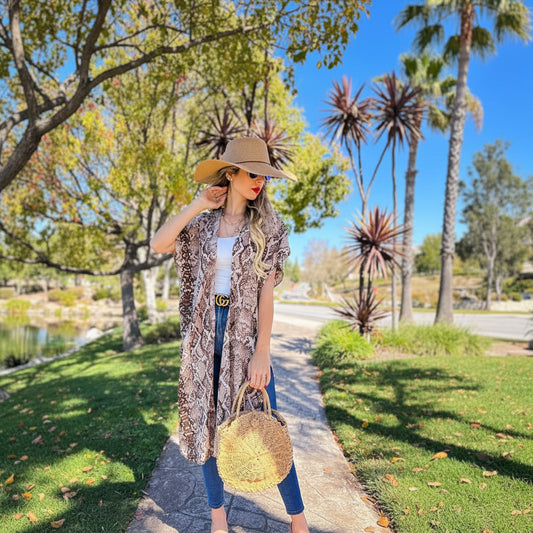 Woman in a snake print cardigan and straw hat walking outdoors on a sunny day.