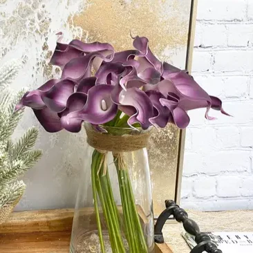 purple flowers arranged in a clear glass vase with brown rope around opening, set on a tray with white brick background