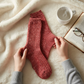 Mellow Monkey strawberry red slub marbled crew socks held by hands on a cozy white blanket with a book and tea