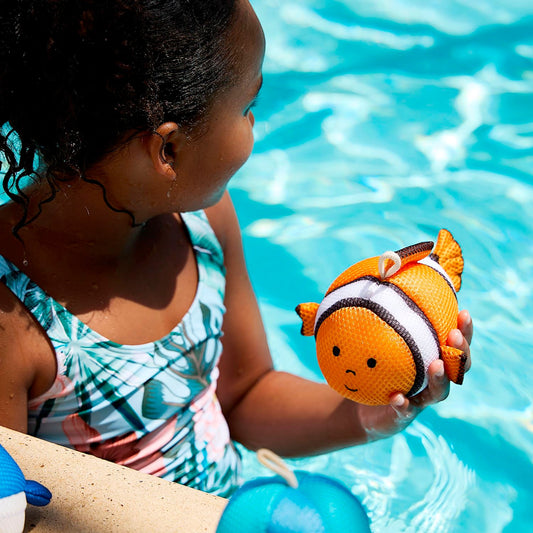 A young child playing in a pool with a clown fish plush bath toy.