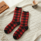 Mellow Monkey red and black buffalo plaid fuzzy crew socks on a cream cable knit blanket with glasses and a diffuser.