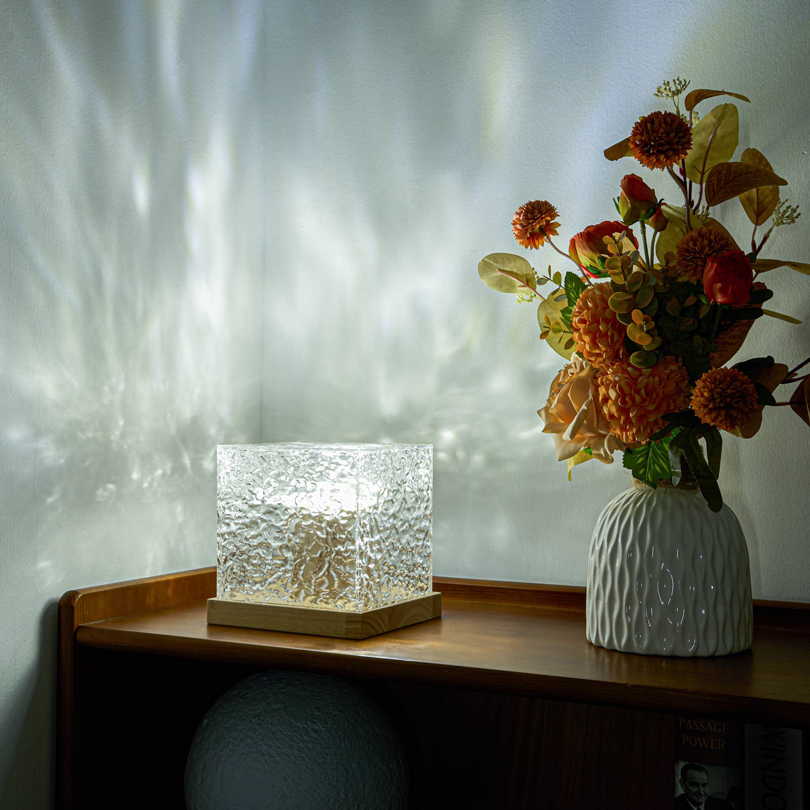 Decorative lamp and vase with flowers on a wooden surface against a textured wall.