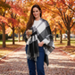 Mellow Monkey Alora open front plaid wrap in black, white, and grey worn by a woman in an autumn park setting.