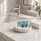 Mellow Monkey Alpine Frost handmade bar soap with blue and white marbled design on a ceramic dish in a bathroom.