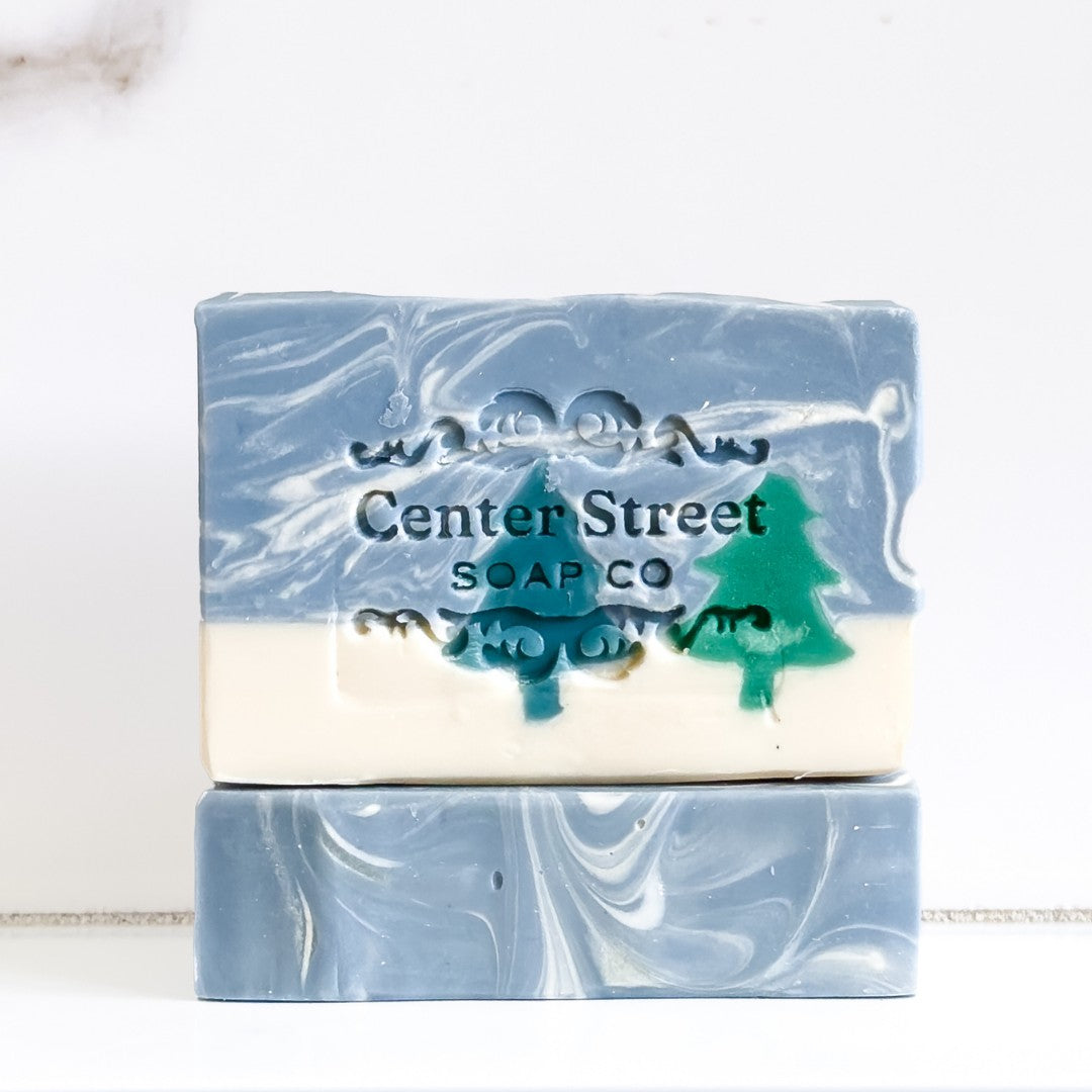 Mellow Monkey Alpine Frost handmade vegan bar soap with a marbled blue and white design and stamped pine tree motif.