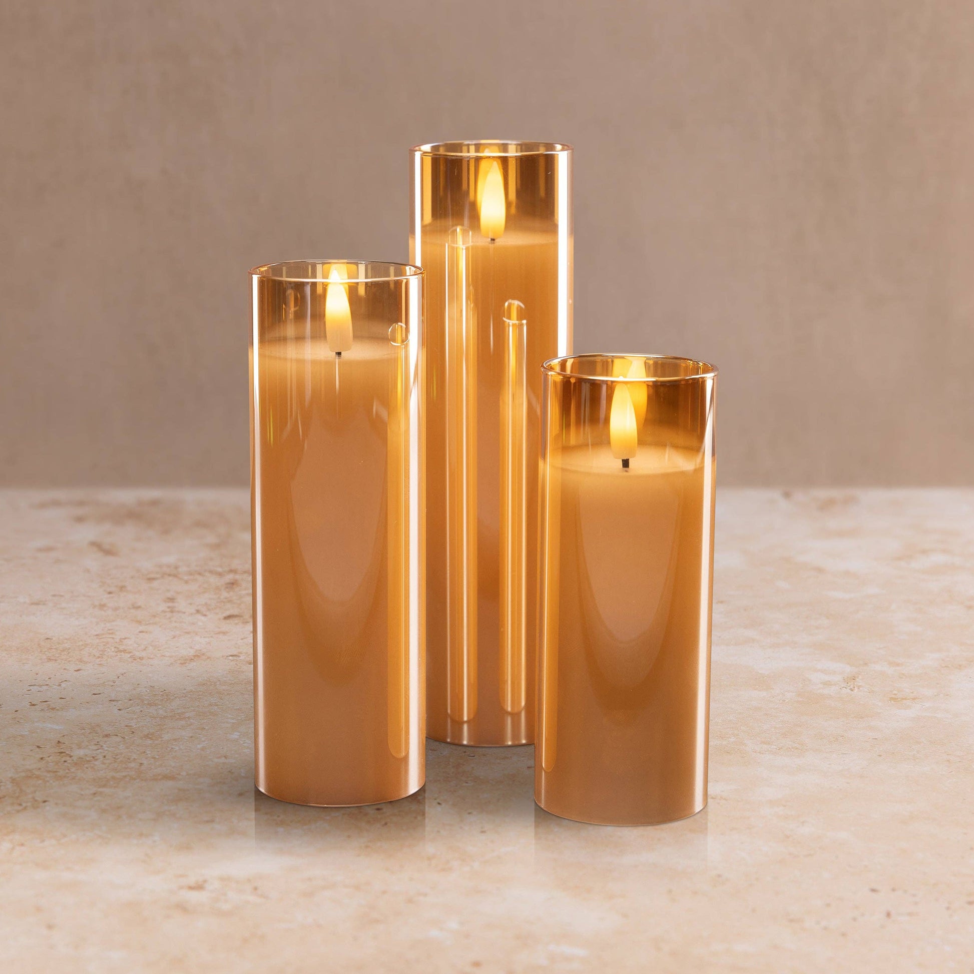 Mellow Monkey set of three amber glass flameless LED pillar candles with a warm flickering glow on a stone surface.