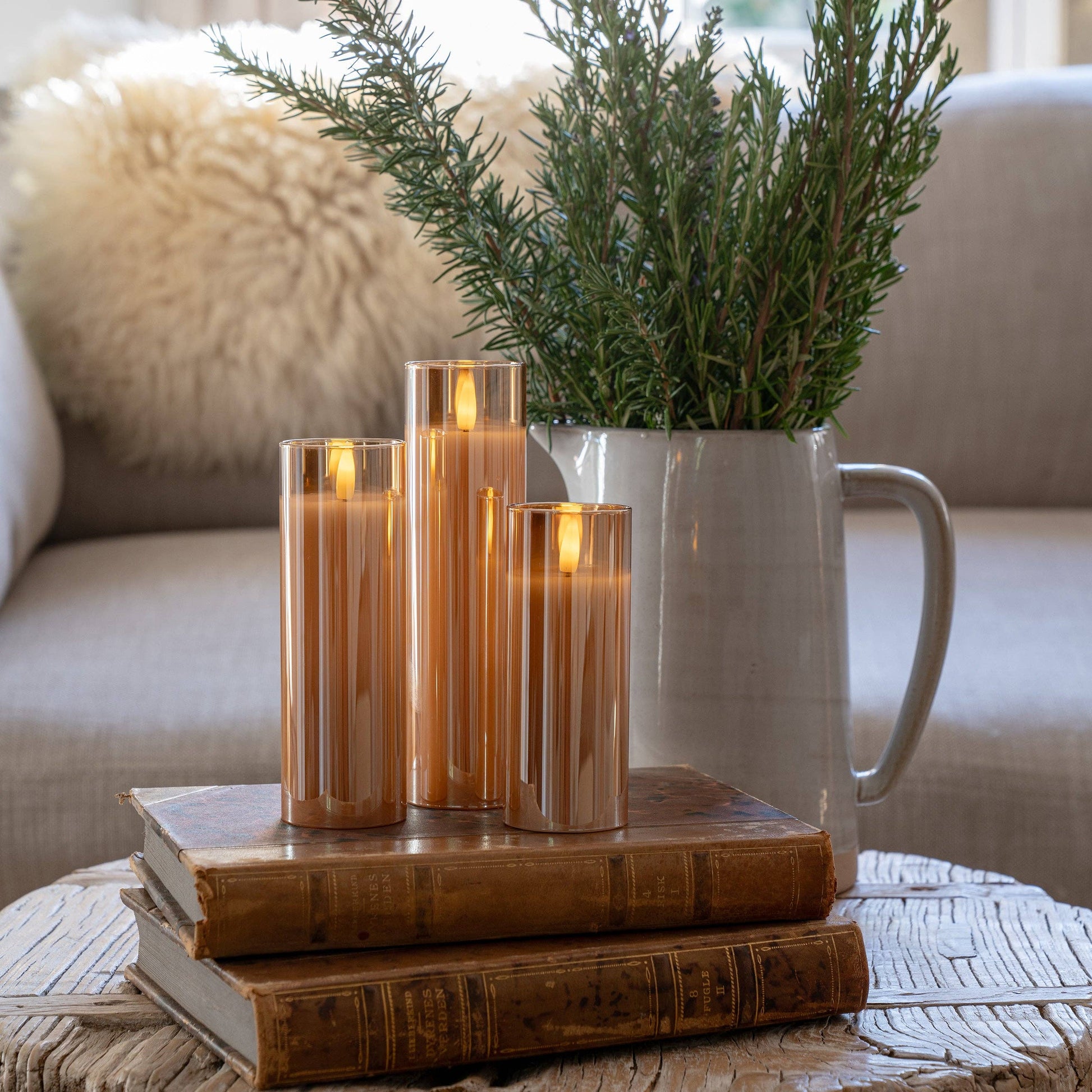 Mellow Monkey set of three amber glass LED flameless pillar candles with a warm glow, displayed on vintage books.