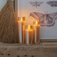 Mellow Monkey set of three amber glass flameless LED pillar candles with warm glowing light on a rustic wooden shelf.