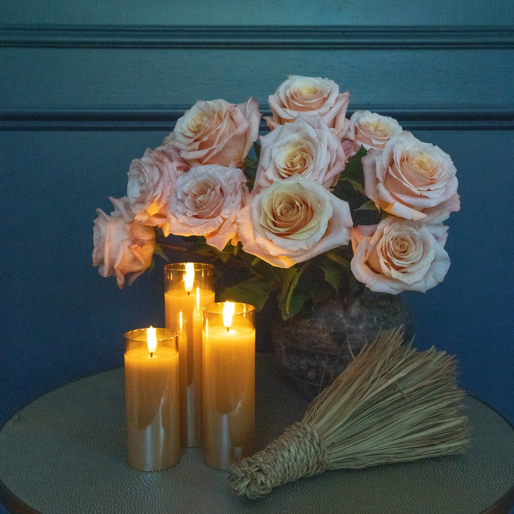 Mellow Monkey amber glass flameless LED pillar candles with flickering glow next to a bouquet of soft pink roses