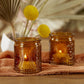 Mellow Monkey vintage amber glass tea light holders with embossed fleur-de-lis patterns on a rustic fabric surface.