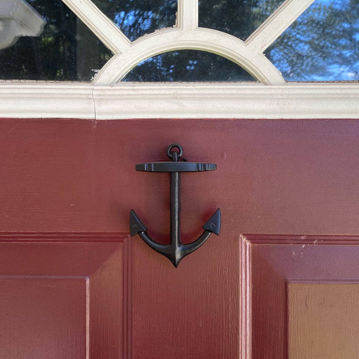 Mellow Monkey handcrafted matte black anchor door knocker mounted on a deep red front door.