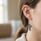Mellow Monkey antique silver cross drop earrings worn on a woman's ear with detailed vintage patina finish.
