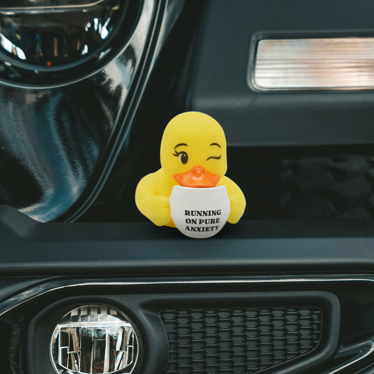 Mellow Monkey yellow rubber duck holding a coffee mug that says Running on Pure Anxiety on a car dashboard