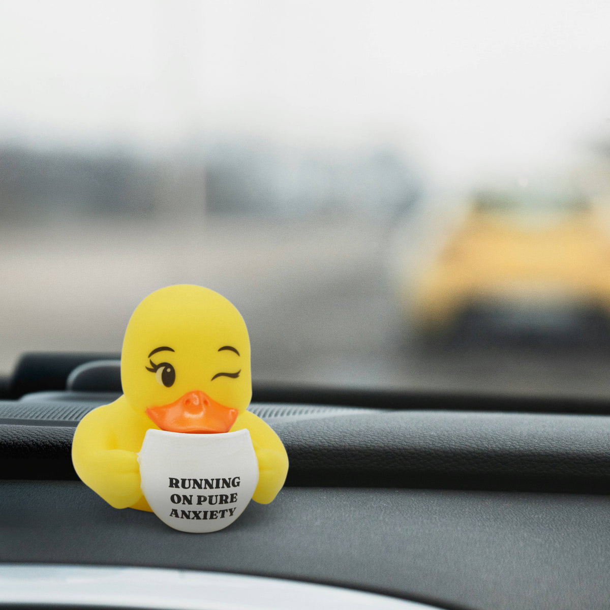 Mellow Monkey yellow rubber duck holding a coffee mug that says Running on Pure Anxiety on a car dashboard