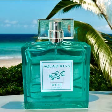 Mellow Monkey Aqua D' Keys West eau de parfum in a teal glass bottle against a tropical beach and palm tree backdrop.