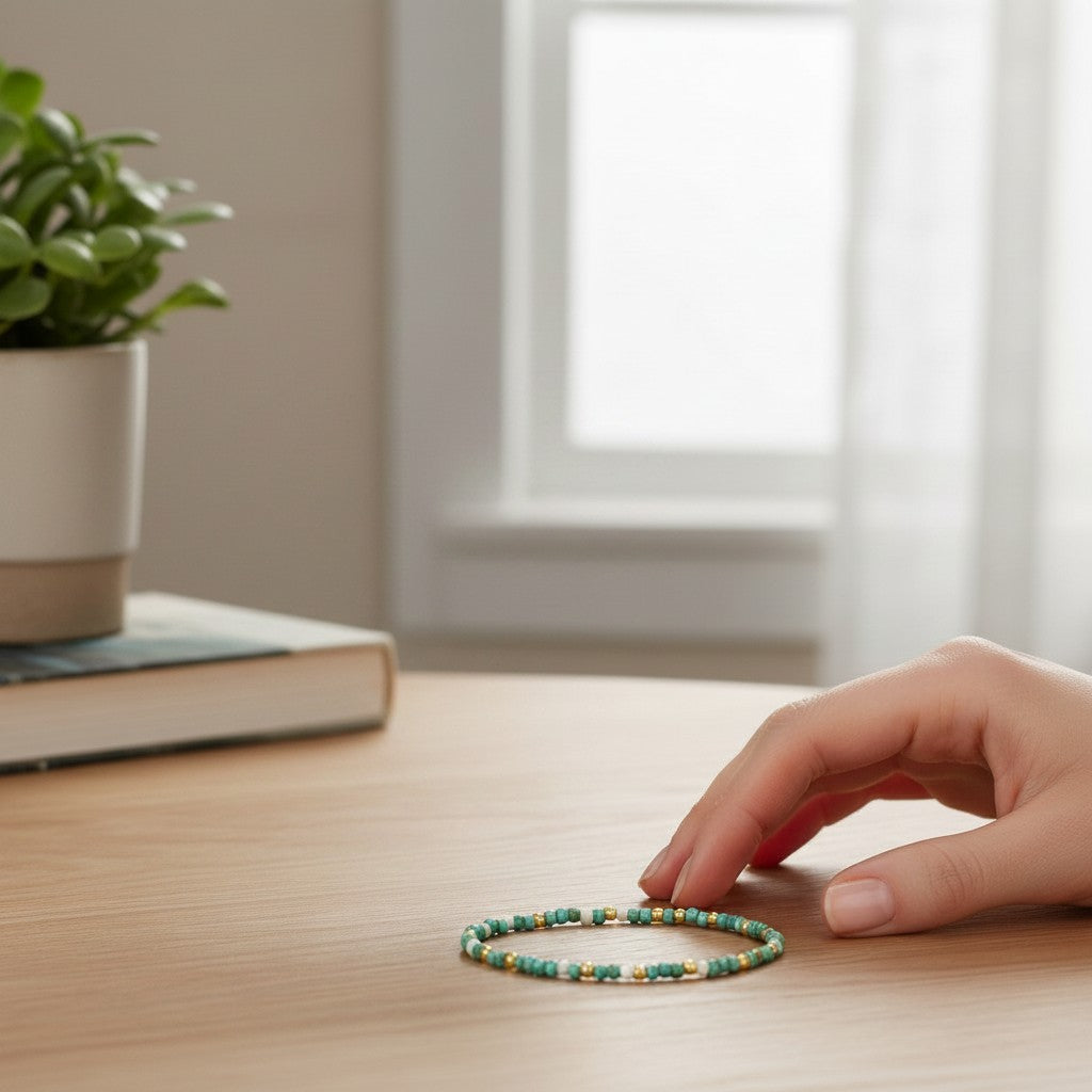 Mellow Monkey stretch seed bead bracelet in aqua and white with 18k gold plated accents on a wooden table.