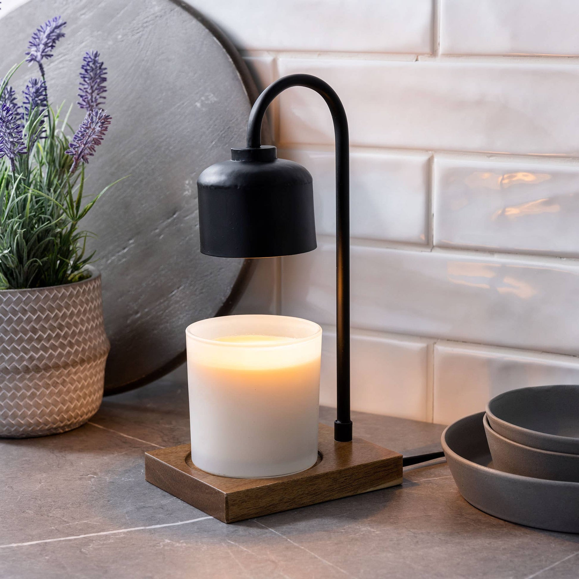 Mellow Monkey black and wood arched candle warmer lamp with a lit jar candle on a kitchen counter.