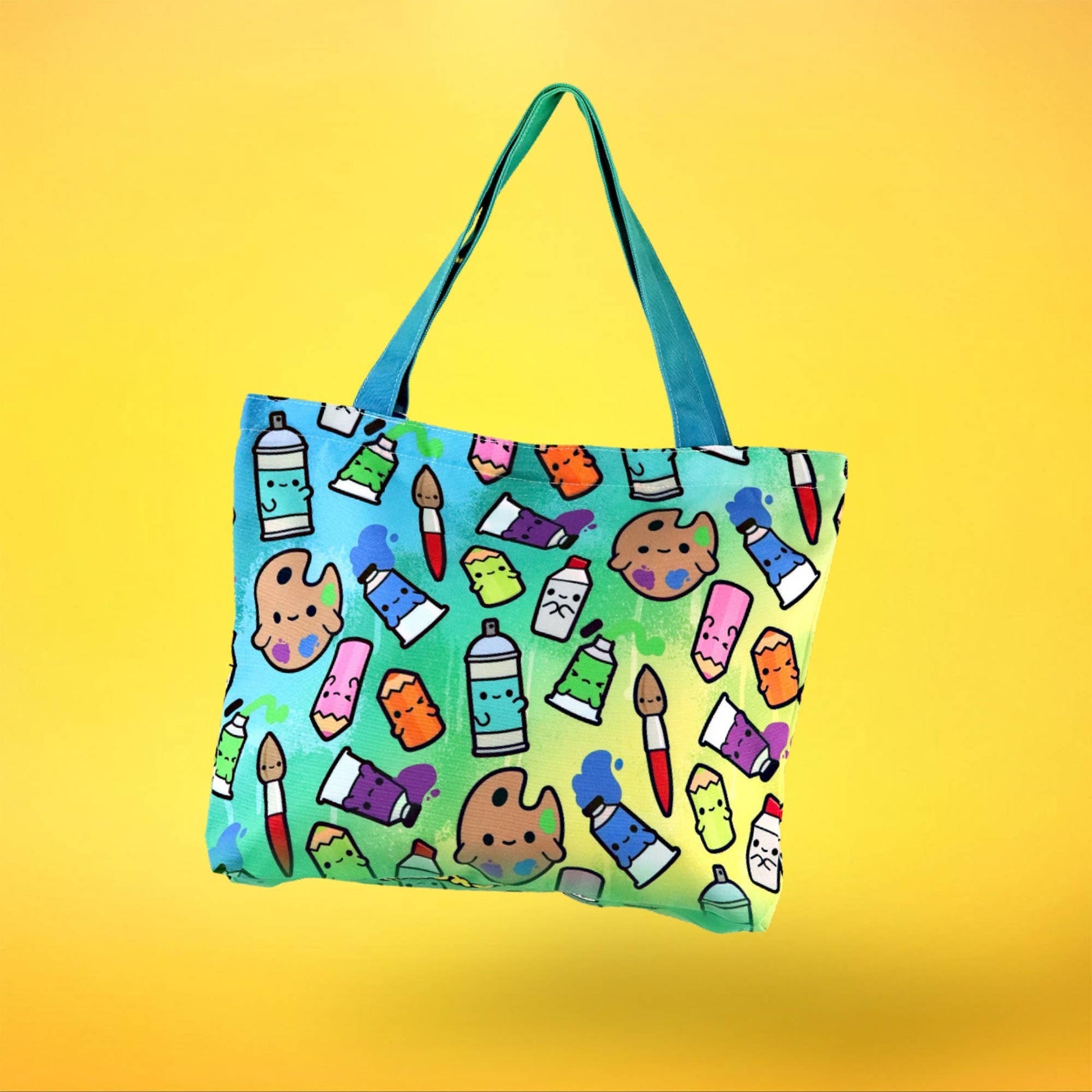Mellow Monkey art supplies tote bag with cute paint tubes, spray cans, and palettes on a gradient background. Features teal straps and a zippered closure.