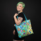 Mellow Monkey art supplies tote bag with paint tubes, palettes, and brushes on a rainbow gradient background. Features dual straps and a zippered closure.