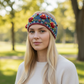 Mellow Monkey Aubrey headband in denim blue wool with hand-knit floral embroidery worn by a blonde woman outdoors.