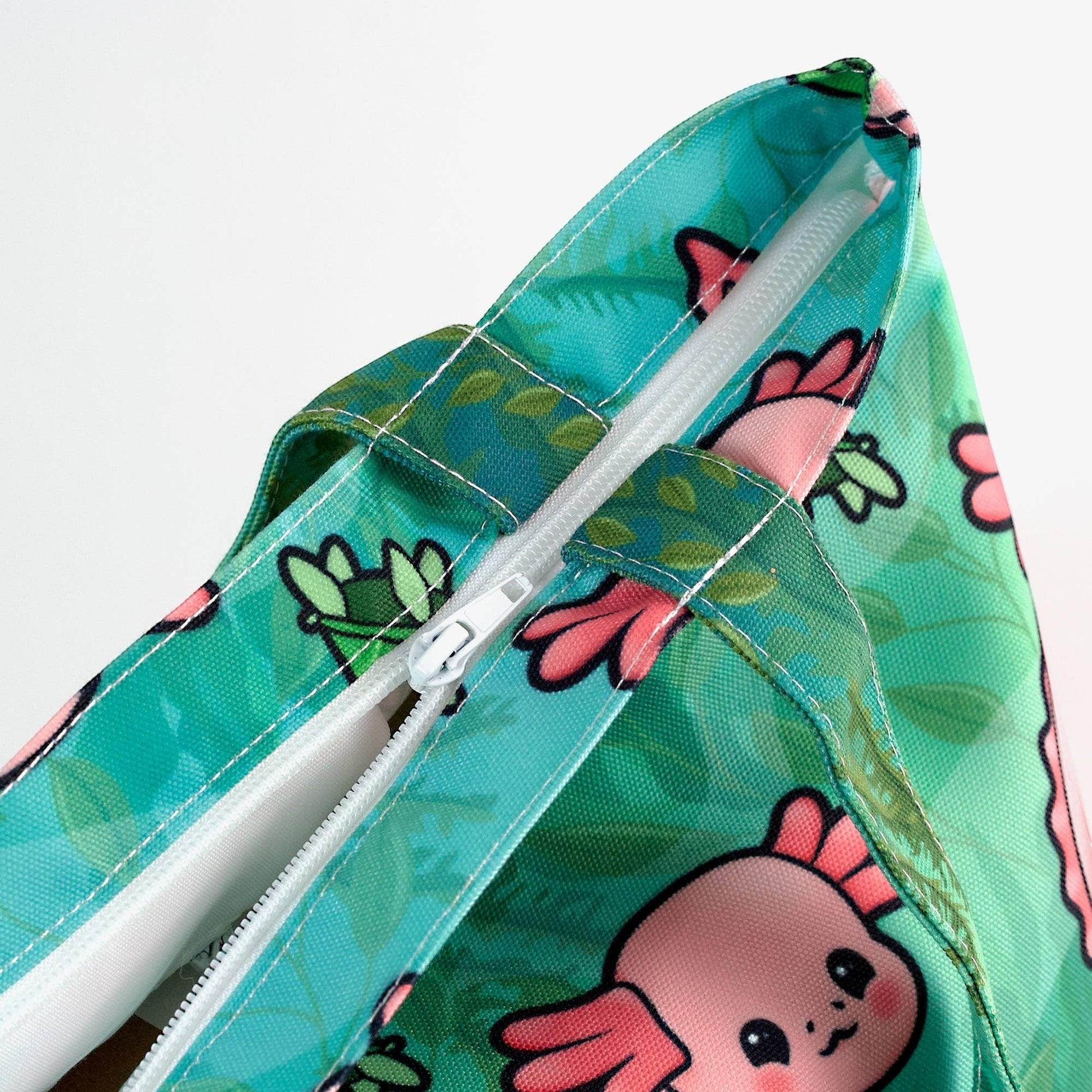 Mellow Monkey Axolotl tote bag in teal with pink axolotl and floral print, featuring a white zipper closure and dual straps.