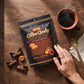 Mellow Monkey Bali's Best coffee candy bag with individual wrappers, a cup of hot coffee, and a hand on a wood table.
