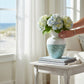 Mellow Monkey 14-inch bamboo and capiz shell vase with blue mosaic and white top, holding hydrangeas on a side table.