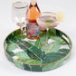 Mellow Monkey banana leaf round resin serving tray with gold trim, featuring a tropical green leaf print on white.