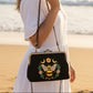 Mellow Monkey Bee Kisslock Bag featuring a black cotton-linen blend with floral, bee, and lunar embroidery on a beach
