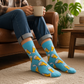 Mellow Monkey bamboo knit socks in sky blue with a beer glass pattern, worn by a person sitting on a leather sofa.