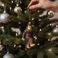 Mellow Monkey hand-painted glass Bigfoot ornament in brown and gold with glitter accents hanging on a Christmas tree.