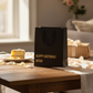 Mellow Monkey black heavy-duty gift bag with gold foil Happy Birthday Bitch text on a wooden table with cake