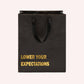 Mellow Monkey black heavy-duty kraft paper gift bag with gold foil Lower Your Expectations text and cotton handles