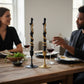 Mellow Monkey black twig-shaped taper candles with gold snake detail, set of two on a dining table with wine glasses.