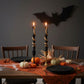 Mellow Monkey black and gold twig taper candles with snake detail, lit on a Halloween decorated dining table.