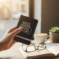 Mellow Monkey Silly Goose Social Club black leatherette pocket journal held in hand near a coffee cup and book.
