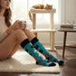 Mellow Monkey light blue crew socks featuring a repeating cartoon cat pattern, worn by a woman sitting at home.