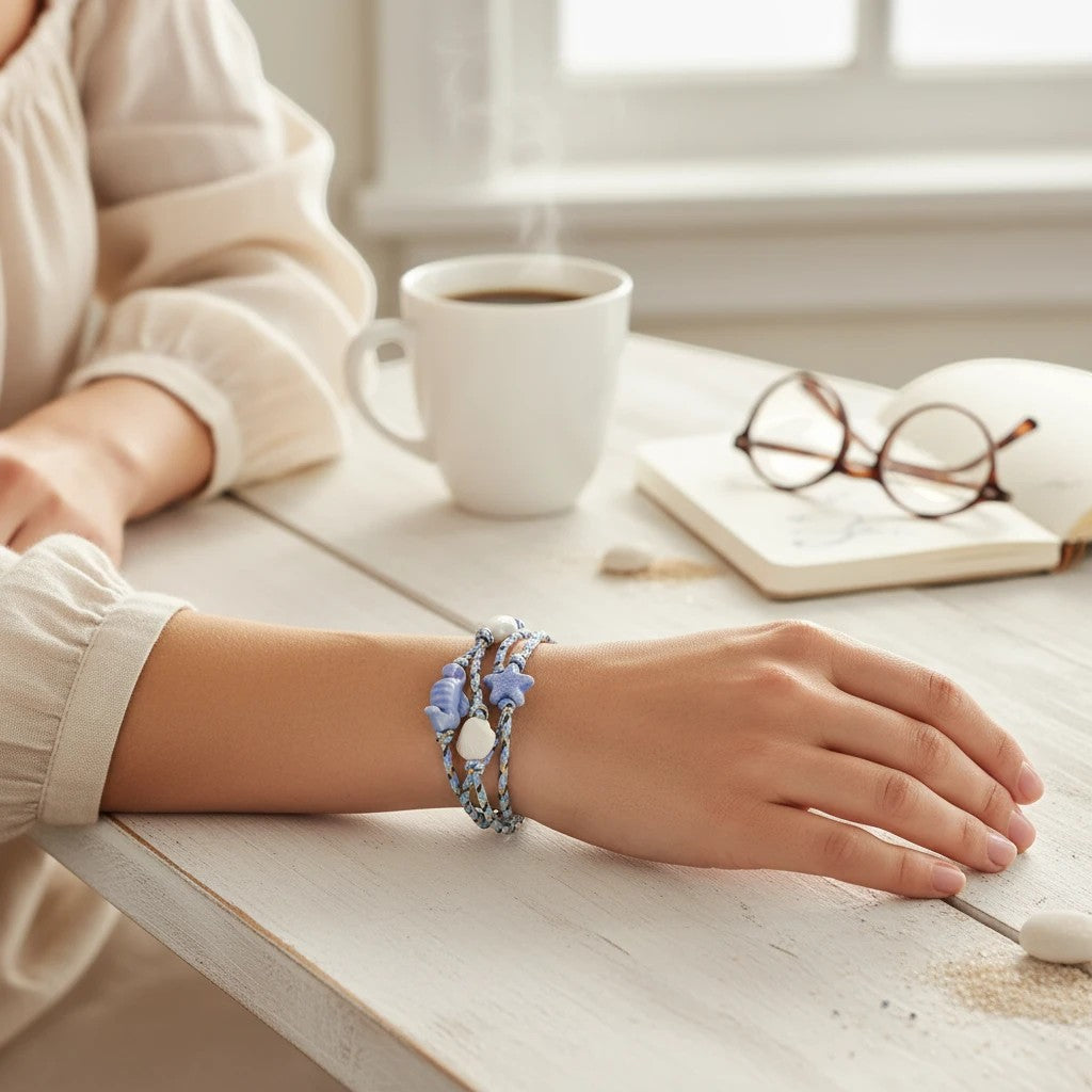 Mellow Monkey blue cord bracelet featuring sea-themed charms worn on a wrist at a desk with coffee and a book.