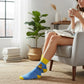 Mellow Monkey blue crew socks with a rubber duck graphic and What The Actual Duck slogan, worn by a woman in a chair.