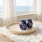 Mellow Monkey Temp-tations blue stoneware salt and pepper shakers with white floral lace pattern on a wooden tray.