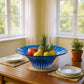 Mellow Monkey hand-painted blue glass centerpiece bowl filled with fresh fruit on a wooden dining table.