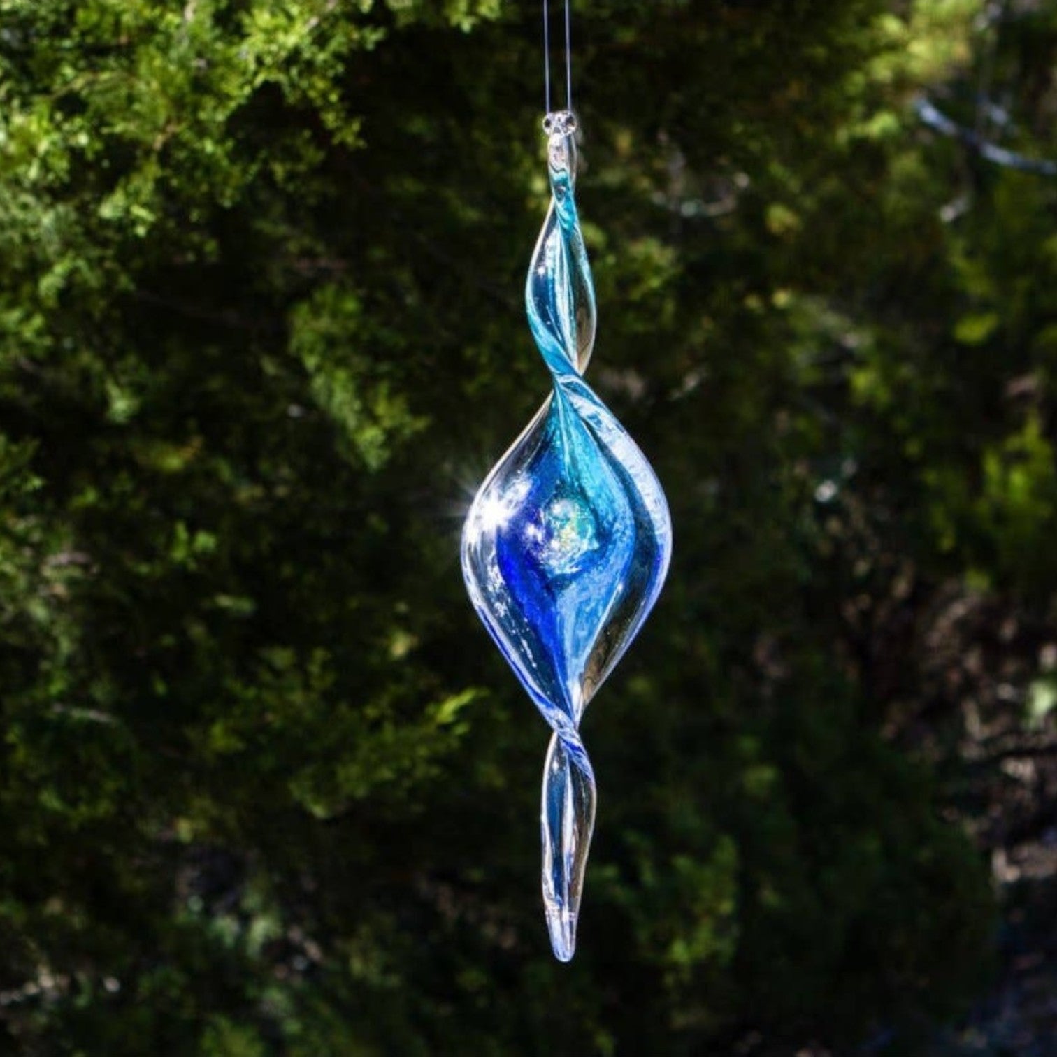 Mellow Monkey 7-inch hand-blown glass spiral ornament in shades of blue, hanging outdoors to catch the sunlight.