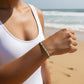 Mellow Monkey blue, mint, and white seed bead stretch bracelet with 18k gold-plated accents worn on a beach.