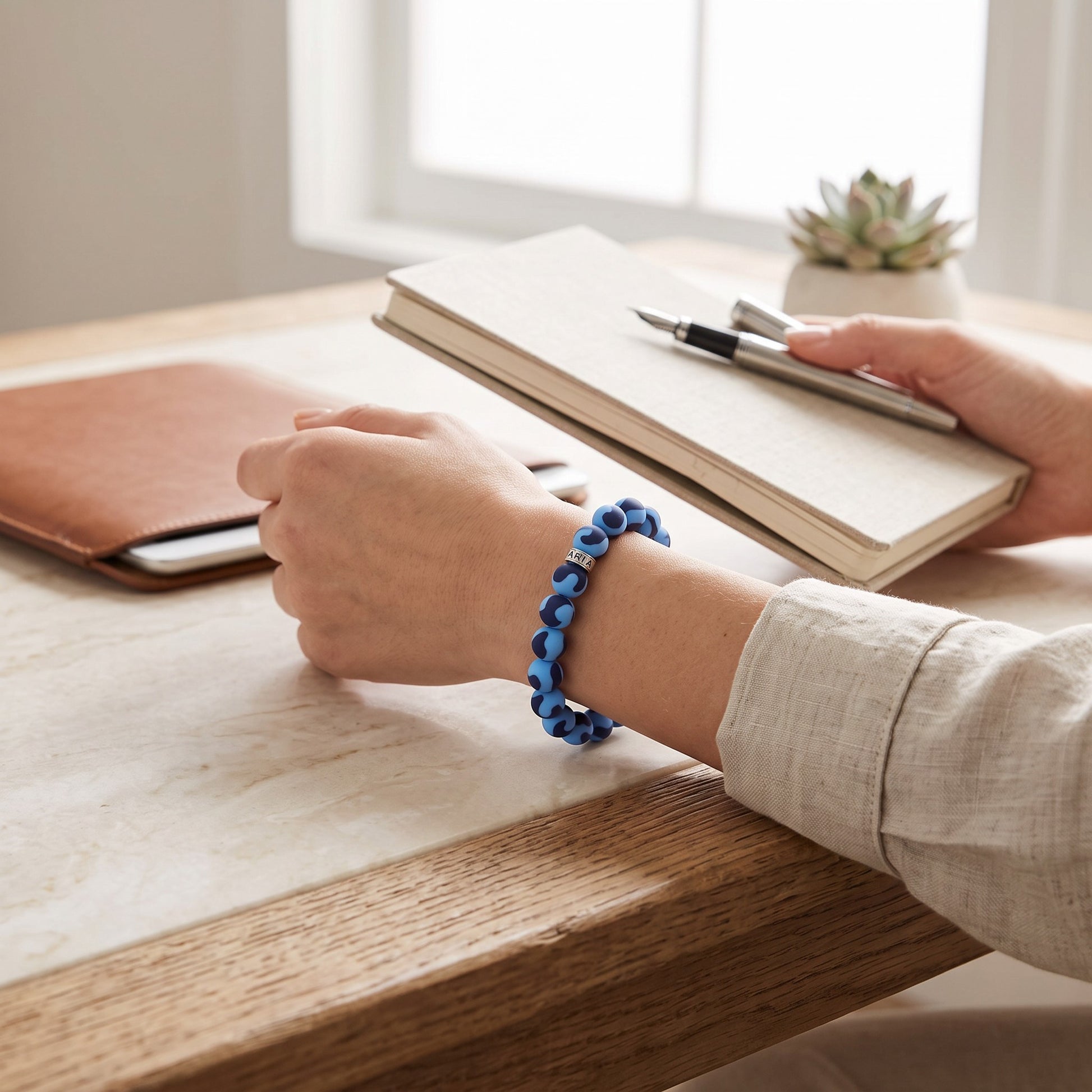 Mellow Monkey light blue and navy matte bead bracelet with silver accent on a person writing in a notebook.